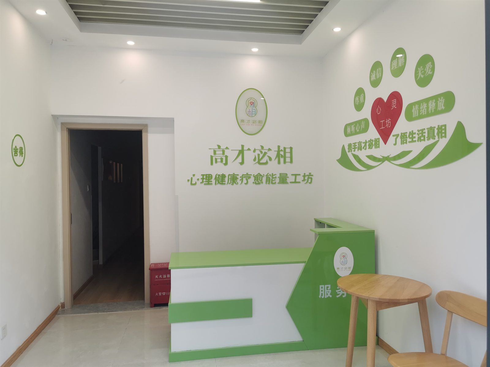 工作室门厅,白墙上为高才宓相标识与「心理健康疗愈能量工坊」字样,右侧是绿色服务台与木质圆桌