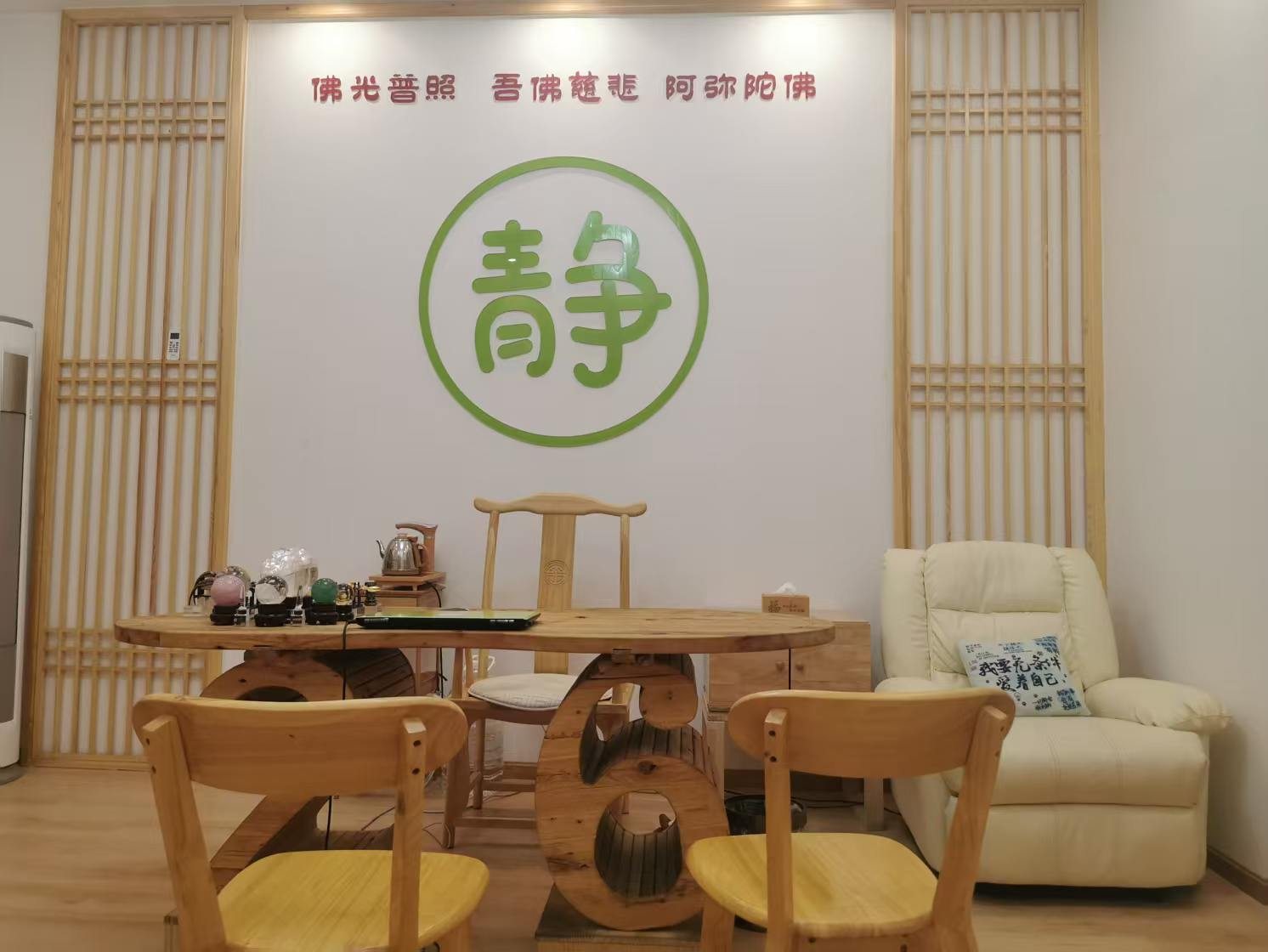 木质格栅之间的白墙上是一面绿色「静」字,前方为原木茶桌与座椅